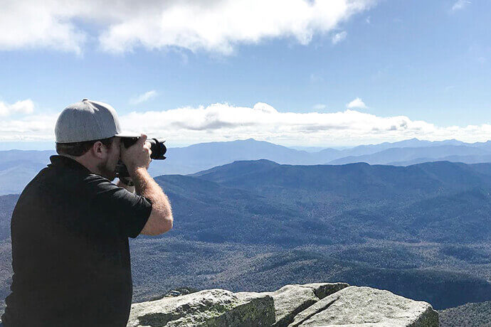 photo of man in black shirt and gray hat taking pictures with camera of a scenic mountain landscape